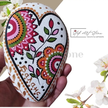 Ръчно рисуван камък във формата на сърце с ярки орнаменти, бял фон и златен надпис „Баланс“. Подходящ за декорация или подарък с послание.