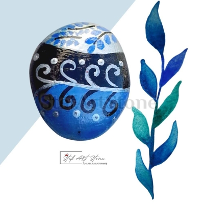  Ръчно рисуван камък в сребристо, синьо и черно, разположен на дървена полица в съвременен интериор.