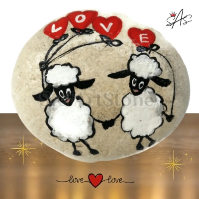 Ръчно рисувано морско камъче с изобразени две овчици, хванати за ръка, украсено със сърца и надпис „LOVE“. Уникална декорация и романтичен подарък.